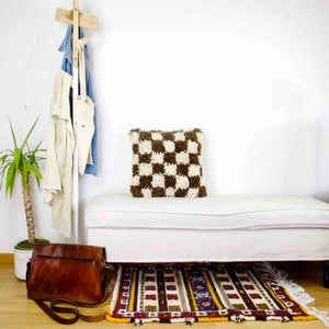 Brown checkered Moroccan Berber pillow standing on a white bench.