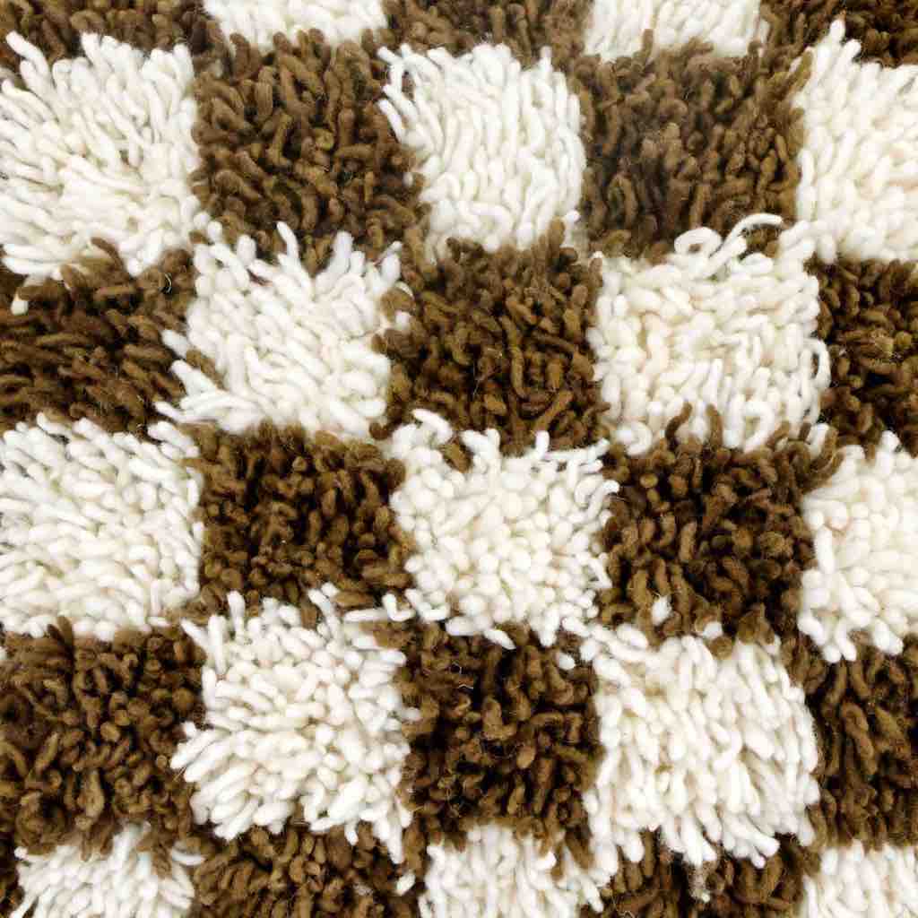 Detailed zoom of the wool texture of a brown checkered Moroccan Berber pillow in front of a white background.