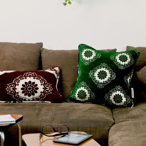 Burgundy red and emerald green decorative pillows on a brown couch.