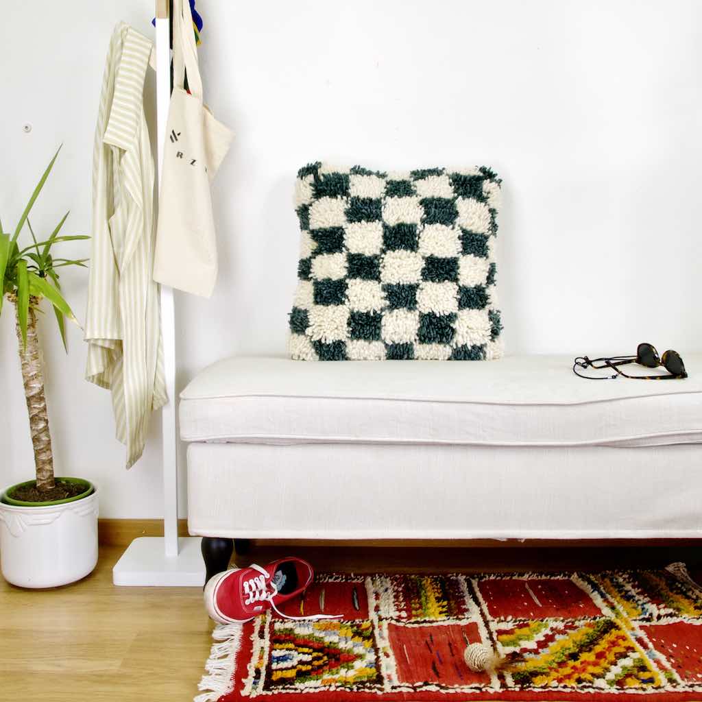 Checkered Moroccan Fluffikon pillow standing on a white bench.