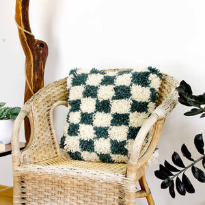 Checkered Moroccan Fluffikon pillow standing on a rattan chair.