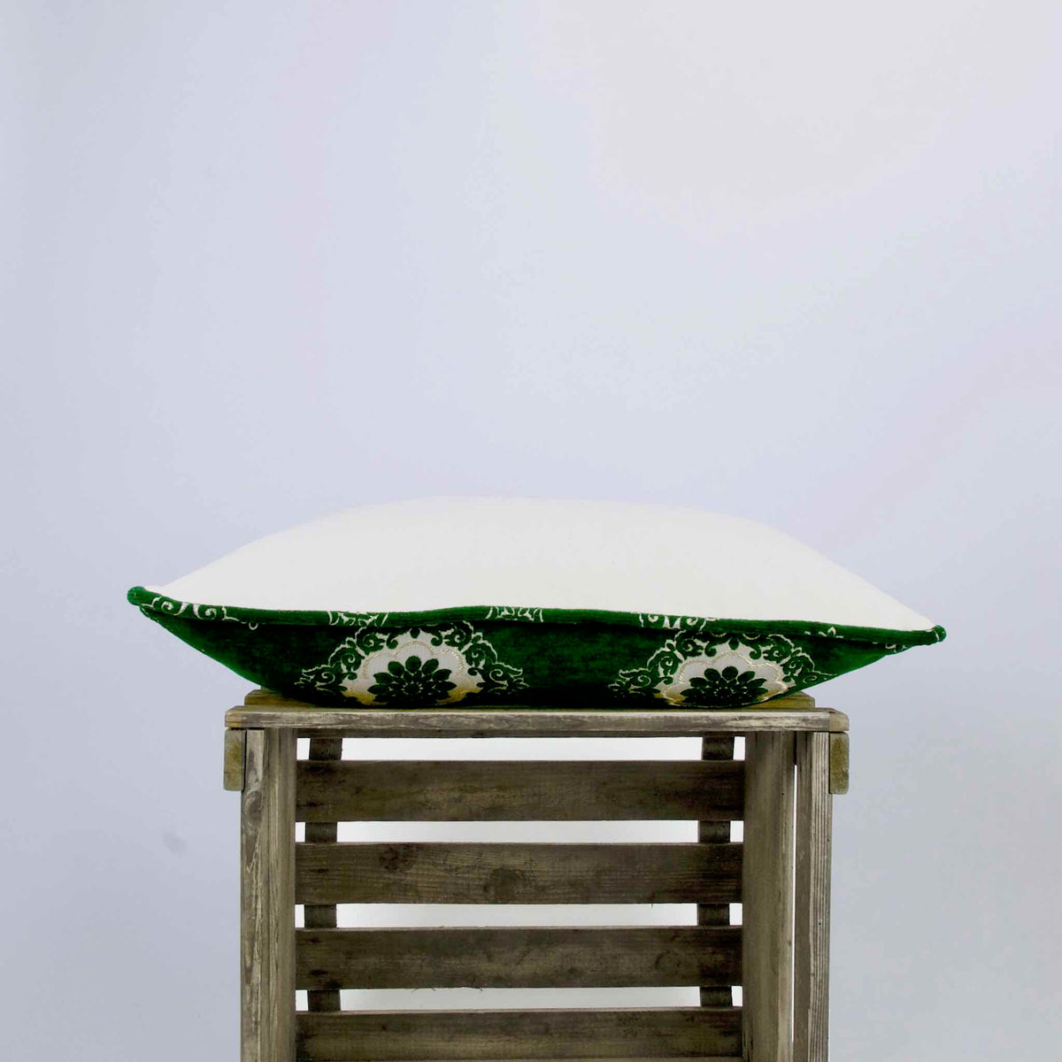 Emerald green velvet pillow lying on a wooden box.