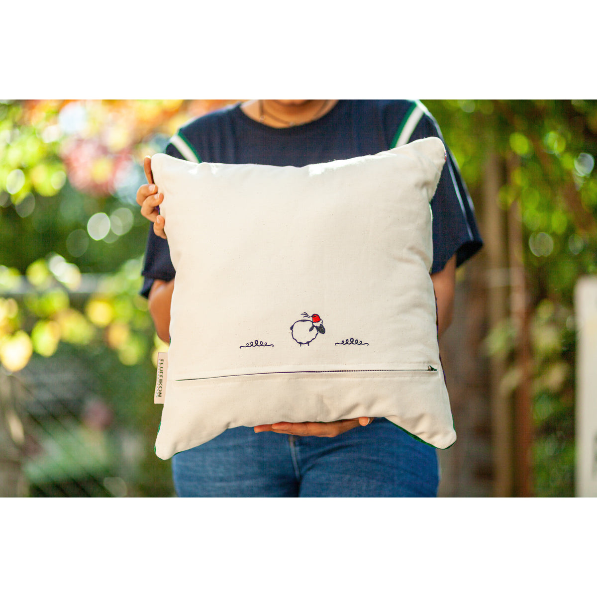 Fluffikon brown green decorative pillow with colourful berber symbols. It is made from a unique handmade thread rug shown from the back held by a woman.