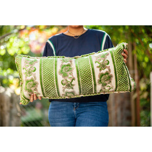 Fluffikon velvet lumbar pillow. Grey and green colours with flowers on it. Pillow shown from the front held by a woman. Size 35x70 cm.