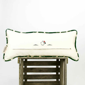 Green velvet lumbar pillow with piping on the pillow edges standing on a wooden box.