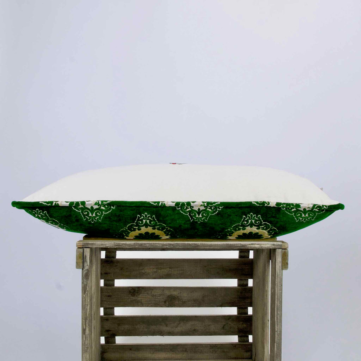 Green velvet lumbar pillow lying on a wooden box.