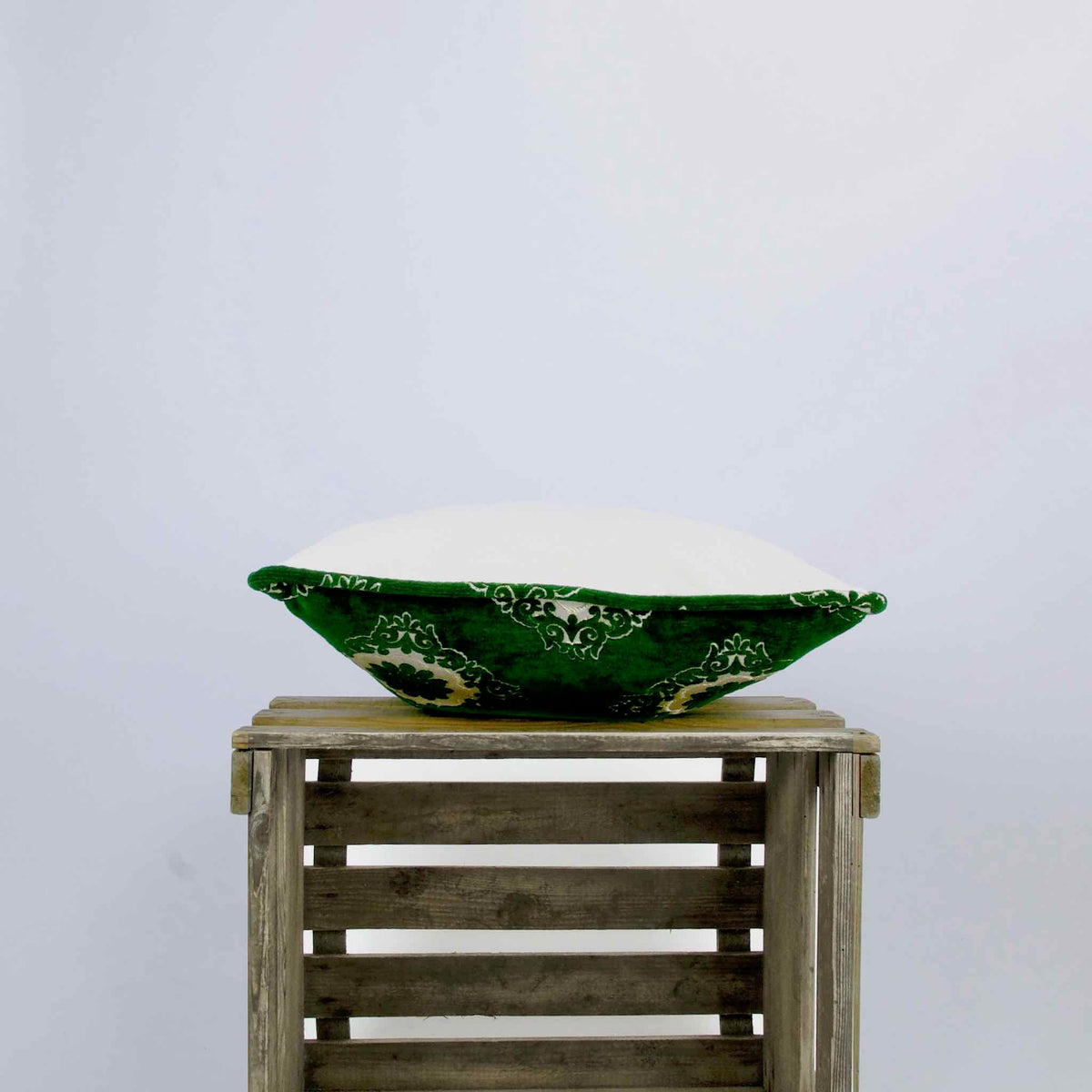 Side view of a green velvet throw pillow on a wooden box.