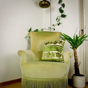 Green velvet throw pillow on a green chair. A palm plant stands next to the chair.