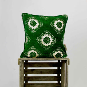 Green velvet throw pillow with piped edges on a wooden box