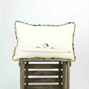 Large decorative Fluffikon pillow with piped edges on a wooden box. The pillow is made from velvet fabric.