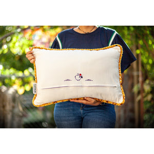 Fluffikon velvet rectangular pillow made from mustard colour fabric with touches of navy blue, grey, cinnamon, and pine green shown from the back held by a woman.