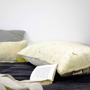Fluffikon oversized lumbar pillow made from beige velvet with golden threads. The pillows is lying on bed with an open book in front of it.