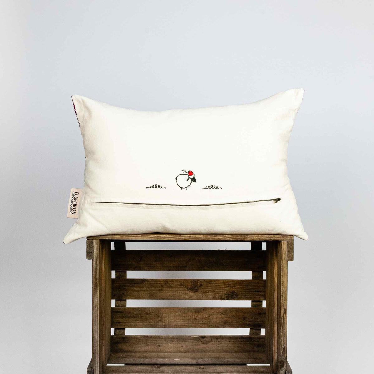 Fluffikon rectangular decorative pillow. The throw pillow is made from pink-white moroccan silk fabric shown from the back on a wooden box.