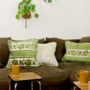 Green square and rectangular velvet pillows on a brown couch.