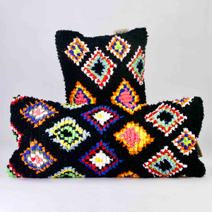 Two black Fluffikon Boucherouite pillows. The Moroccan pillows are made from upcycled clothes. They have colorful patterns in yellow, red, blue and green.