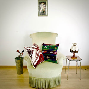 Two decorative Fluffikon throw pillows on an old green velvet chair.