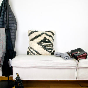 Vintage black and white rug pillow made from a Moroccan carpet. The Berber pillow is standing on a white bench.