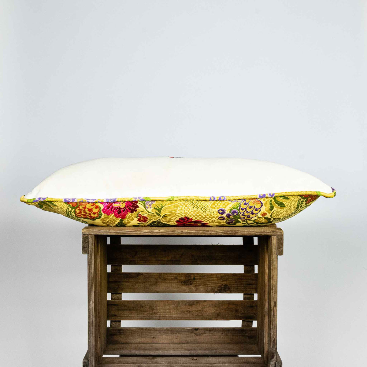 Side of yellow lumbar Brocade pillow on wooden box