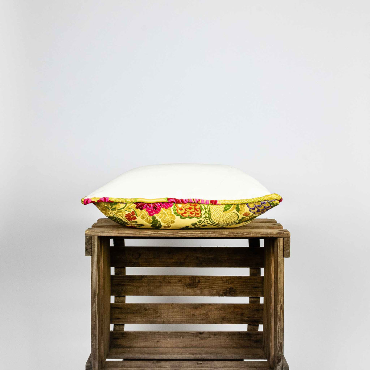 Side of yellow square Brocade pillow on wooden box.