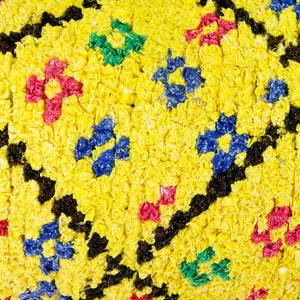 Very close zoom on a yellow Boucherouite lumbar pillow. The Moroccan lumbar pillow has many colorful dots.